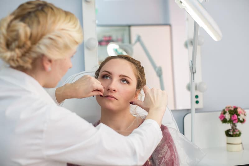 Master corrects makeup, gives shape and thread plucks eyebrows in a beauty salon.